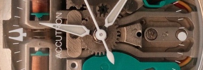 Cropped closeup of the Accutron 214 movement showing exposed wires, cogs, green plastic spaces, and the hands.