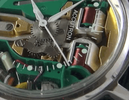 Cropped closeup of the Accutron 214 movement showing exposed wires, cogs, green plastic spaces, and the hands.